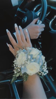 a woman's hand on the steering wheel of a car with white flowers and greenery