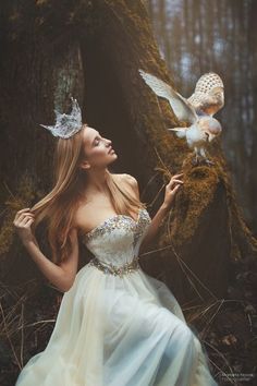 a woman in a white dress standing next to a tree with an owl on her shoulder