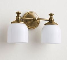 two light bathroom fixture in brass finish with white glass shades on the bulbs and sides