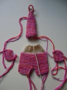 a knitted doll with pink and white clothing on it's back, next to a pair of knitting needles