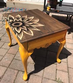 a wooden table with a sunflower painted on it's top sitting on a brick sidewalk