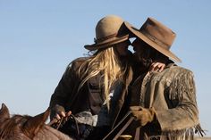 two people riding on the back of a brown horse next to a man in a cowboy hat