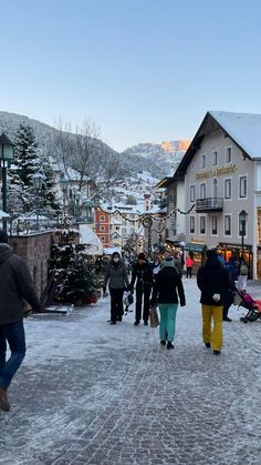 several people walking down a snowy street in front of buildings and trees with snow on the ground