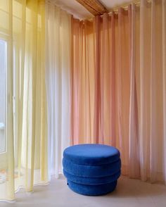 a blue ottoman sitting in front of a window with sheer curtains on the outside wall