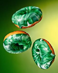 three doughnuts with green and white icing on them sitting in front of a yellow background