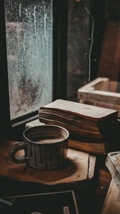 a cup of coffee sitting on top of a wooden table next to an open book