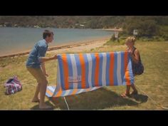 two people holding up a blue and orange striped beach towel near the water's edge