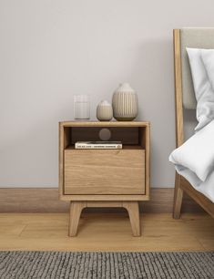 a nightstand with a book and vase on it next to a bed