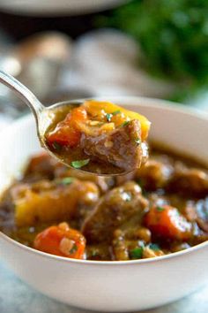 a spoon full of beef stew with carrots and parsley on the side in a white bowl