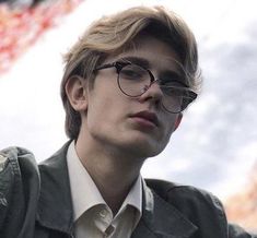 a young man wearing glasses standing in front of an american flag and looking off into the distance