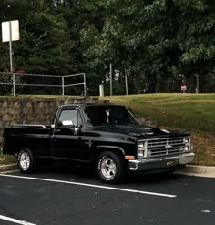 a black pickup truck parked in a parking lot next to a stone wall and trees