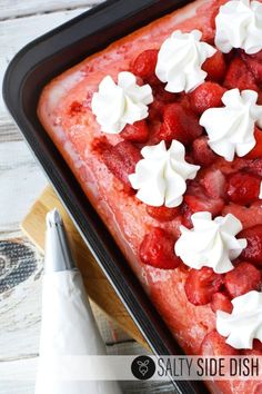 strawberry poke cake with whipped cream on top in a baking pan, ready to be eaten