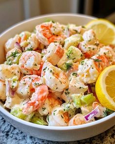 a white bowl filled with shrimp salad next to a lemon wedge on top of a table