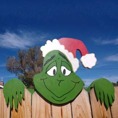 a wooden fence with a green grin face and santa hat on it's head