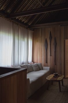 a living room with wood paneling and white curtains on the window sill, next to a coffee table