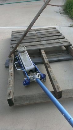 a wooden pallet with a blue hose attached to it and a piece of wood on the ground