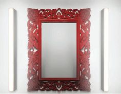 a red mirror sitting on top of a white wall next to two mirrors and lights