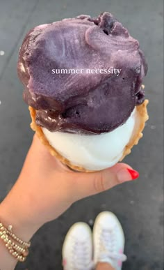 a person holding an ice cream cone with purple icing and white frosting on it