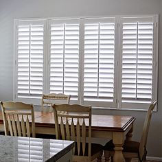 a dining room table and chairs in front of white shuttered windows with marble counter tops