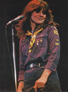 a woman with long hair standing in front of a microphone and wearing an army uniform