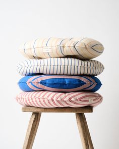 four pillows stacked on top of each other in different colors and sizes, sitting on a wooden stool