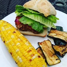 a plate with a sandwich, corn on the cob and grilled eggplant