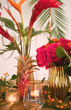 a table topped with vases filled with flowers and pineapples next to candles