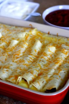 a red casserole dish with cheese and other food items in bowls on the side