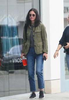 a woman walking down the street carrying a red cup and talking to another woman in front of a store