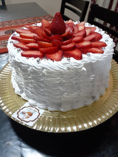 a white cake topped with strawberries on top of a gold platter next to a table