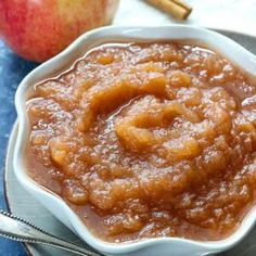 a bowl filled with apple sauce next to an apple and cinnamon stick on a plate