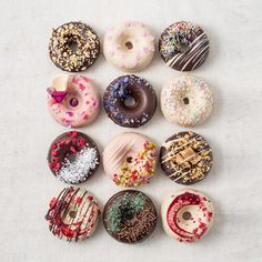 there are many different types of donuts on this white tablecloth, including one with frosting and sprinkles