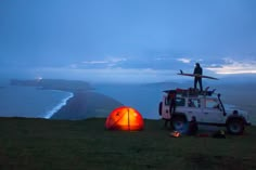 a man standing on top of a vehicle next to a tent with a surfboard