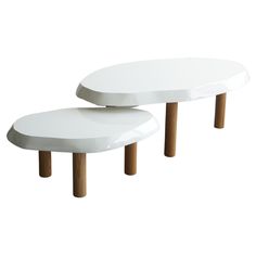 two white tables with wooden legs on each side, one is shaped like an oval table