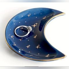 a blue moon shaped dish with a wedding ring on it's side and gold stars around the edge