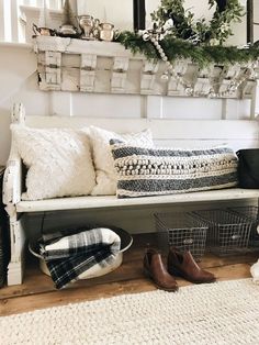 a white bench with pillows and blankets on it in front of a mirror, basket filled with christmas wreaths