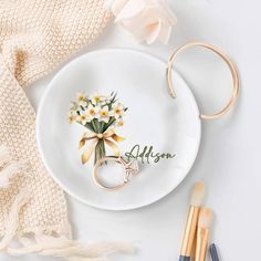 a white plate topped with a bouquet of flowers next to two brushes and a pair of scissors