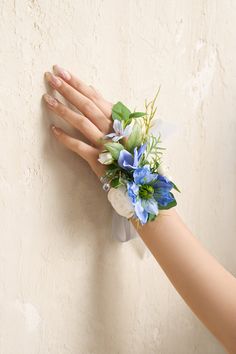 a woman's hand holding a bouquet of blue and white flowers against a wall