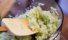 the food processor is full of green vegetables and rice flakes, with a wooden spoon in it