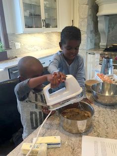 two young boys are making food in the kitchen while one boy is using an electric mixer