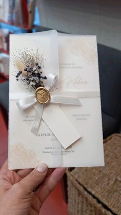 a person holding up a wedding card with a ribbon and flower on the front pocket