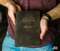 a man holding a brown leather book with the word tom on it in his hands