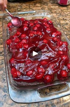 someone is spooning cherries from a cake in a glass dish on a counter