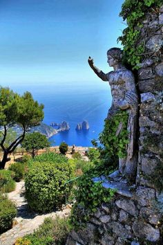 a statue on the side of a stone wall with trees and water in the background