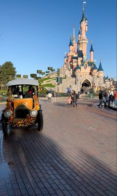 an orange car driving down a brick road in front of a castle