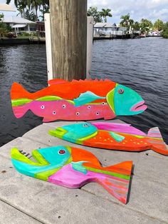 two colorful fish sitting on top of a pier next to the water with palm trees in the background