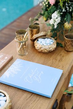 a wooden table topped with a blue book next to a vase filled with flowers and candles