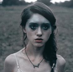 a woman with black makeup standing in a field