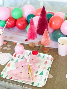 the table is set with pink, green and red christmas tree decorations on top of it