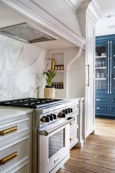 a white kitchen with marble counter tops and gold trim on the oven hood, along with blue cabinets